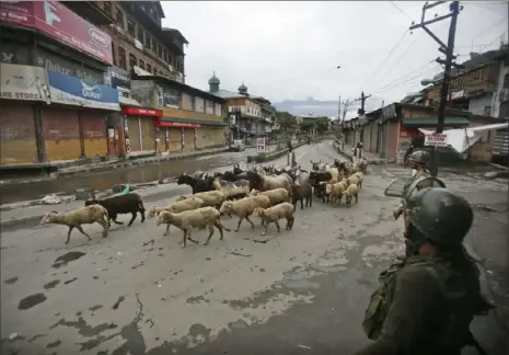  ?? Mukhtar Khan/Associated Press ?? Indian paramilita­ry soldiers stand guard as a livestock seller crosses a street Saturday, ahead of the Eid al Adha holiday during a security lockdown in Srinagar, Indian-controlled Kashmir.