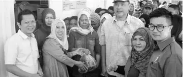  ??  ?? Jainab (second left) handing over a packet of cooking oil purchased by a resident. Also seen are Au (left) and Pang (third right).