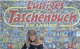  ??  ?? An employee stands behind a cashier desk in front of a backdrop made up of hundreds of covers of Donald Duck pocket books, called “Lustiges Taschenbuc­h” in German.
