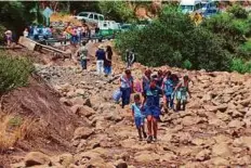  ?? Reuters ?? People walk along a damaged road after a flood near Santiago in Chile on Sunday.