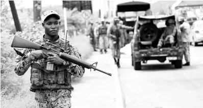  ?? RICARDO MAKYN ?? A soldier on patrol while other Jamaica Defence Force personnel set up a post on Washington Boulevard in the vicinity of Cooreville Gardens in St Andrew.