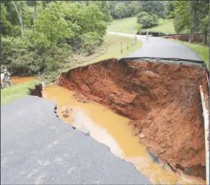 ?? The Associated Press ?? EXPOSED BY RAINS: Pipes and wires are exposed after a culvert washed out a section of road on near Charlottes­ville, Va., on Thursday following heavy overnight rains.