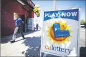  ?? AP PHOTO/GREGORY BULL ?? A man walks by a sign for the lottery in front of a market on Tuesday in San Diego.