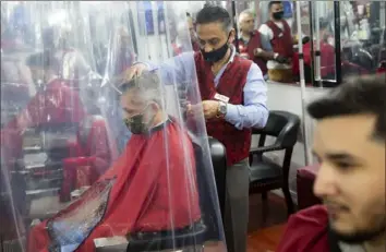  ?? John Minchillo/Associated Press ?? Peter Shamuelov, center, wears a protective mask as he gives a haircut to a customer at Ace of Cuts barbershop in New York on Monday.