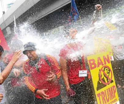  ?? —MARIANNE BERMUDEZ ?? Anti-Trump protesters trying to march toward PICC are hosed down by firemen at the corner of Padre Faura Street and Taft Avenue in Manila on Monday morning.