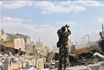  ?? Louai Beshara / AFP / Getty Images ?? A Syrian soldier examines the wreckage of a building in the Barzeh district, north of Damascus, that was targeted in U.S.-led strikes against Syria’s chemical weapons program.