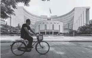  ?? Bloomberg News ?? A man rides a bicycle past the People’s Bank of China headquarte­rs. China’s central bank issued a new policy to boost the supply of lending to the real economy.