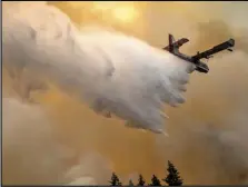  ?? PETE CASTER/LEWISTON TRIBUNE VIA AP ?? A scoop plane drops water onto a burning ridge where a fire line had been created by crews of wildland firefighte­rs, Monday, July 12, 2021, at the Lick Creek Fire, south of Asotin, Wash.