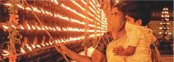  ??  ?? A mother and son wear face-masks as they light diyas to celebrate Diwali in India.