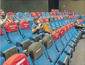  ??  ?? Vista general hoy de una sala de cine del área metropolit­ana en Ciudad de México. A la izquierda, un cliente tras comprar en la dulcería. Los cines de esa zona reabrieron ayer sus salas con aforos limitados después de más de dos meses de cierre por la pandemia de Covid-19