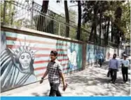  ??  ?? TEHRAN: Iranians stroll by murals on the wall of the former US embassy in the Iranian capital yesterday. — AFP