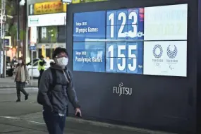  ?? CHARLY TRIBALLEAU/AFP VIA GETTY IMAGES ?? A man wearing a face mask, amid concerns of the COVID-19 coronaviru­s, walks past a display showing a countdown to the start of the 2020 Olympic Games in Tokyo on Monday.