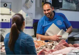  ??  ?? Javi Caña muestra un pargo macho (Dentex gibbosus, Meerbrasse) en su puesto en el mercado Javi atiende a una cliente, “los que compran tres, cuatro, cinco euros..., esos son para mí los grandes clientes”, nos dice. Con uno de sus empleados entrando en la plaza.