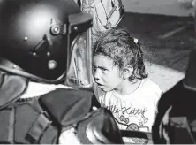  ??  ?? A migrant girl looks at a national guardsmen at the crossing. Authoritie­s estimated that 2,500 migrants were trying to cross.