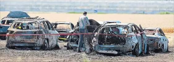  ?? BOB TYMCZYSZYN
THE ST. CATHARINES STANDARD ?? An investigat­or examines wreckage of a fire that caused more than $1 million damage to vehicles parked in a dry field Sunday for the Niagara Lavender Festival.