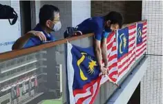  ??  ?? The Malaysian flag is put up at the Games Village in Tokyo by members of the contingent.