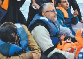  ??  ?? Above: A man who once lived in Baghdad, before moving to Libya, holds his 13month-old daughter as they traverse the choppy waters of the Mediterran­ean Sea en route to Italy on Nov. 17. Below: People wait to grab a rope to be rescued from their wooden...