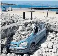  ??  ?? A car under a collapsed building on Kos. Below left, tourists wait outside the terminal at the airport on Kos