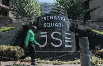  ?? PHOTO: BLOOMBERG ?? A pedestrian passes the entrance to the JSE in Sandton, South Africa. On Friday the country escaped a downgrade to junk status, which would have effected listed companies in the country.