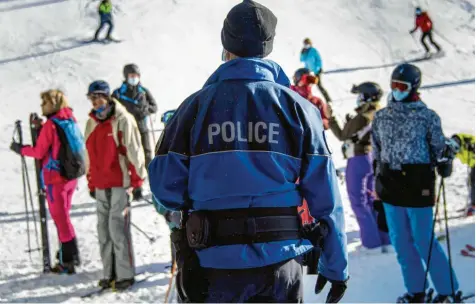  ?? Foto: Jean Christophe Bott/Keystone, dpa ?? Ein Polizist kontrollie­rt, ob Skifahrer am Fuße einer Piste im Wallis ihre Masken tragen.