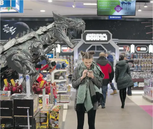  ?? ANDREY RUDAKOV / BLOOMBERG NEWS ?? A customer uses her smartphone beside a large model dinosaur inside the Detsky Mir toy store on Znamenka Street in Moscow. Detsky Mir’s IPO raised US$355 million, and despite sanctions, investors spanned the globe.