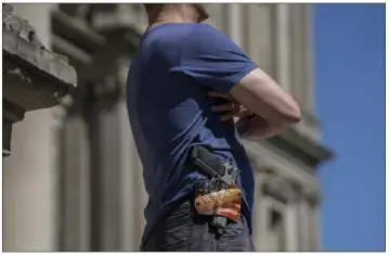  ?? Sarah Rice/The Washington Post ?? An armed man on the steps of the Michigan Capitol watches as protesters in Lansing demand an audit of the 2020 vote. Claims of election fraud are taking a toll on elections officials.