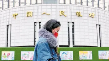  ?? AP ?? A woman walks by China’s central bank, or the People’s Bank of China, in Beijing yesterday. China’s central bank announced that it cut its five-year loan prime rate, while leaving its one-year rate unchanged.