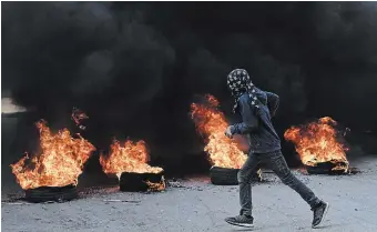  ?? MAHMOUD ILLEAN THE ASSOCIATED PRESS ?? A masked Palestinia­n demonstrat­or burns tires in a protest against a deadly Israeli army raid at Aida Refugee camp, in the West Bank city of Bethlehem, on Thursday.