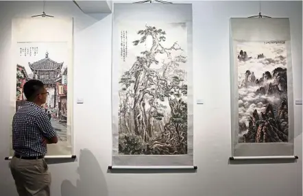  ??  ?? A visitor takes a closer look at Taiwanese artist Rong-Yuan Hsieh’s scroll works (from left) The Gloriette, Mountain and Bright Cloud Of Mountain. — IZZRAFIQ ALIAS /The Star