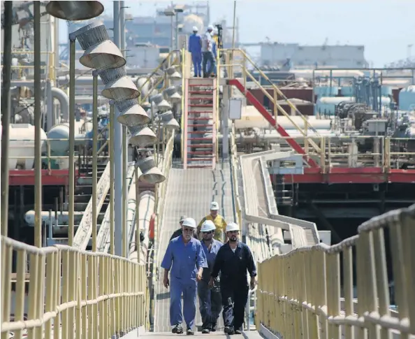  ?? HAIDAR MOHAMMED ALI/AFP/GETTY IMAGES ?? Iraqi labourers walk past an oil tanker docked at a floating platform offshore from the southern Iraqi port city of Al Faw. Neighbouri­ng Iran could swell the glut if restrictio­ns on its sales are removed with the completion of a nuclear accord.