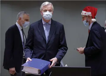  ?? OLIVIER HOSLET ?? A colleague wears a Christmas hat as European Union chief negotiator Michel Barnier, center, carries a binder of the Brexit trade deal during a special meeting at the European Council building in Brussels on Friday.