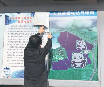  ?? — WP-Bloomberg photo by Emily Rauhala. ?? Dou Yongqiang, a 29-year old engineer, fixes a sign at Panda Green Energy’s panda-shaped plant in Datong, China and (below left) Panda Green Energy’s panda-shaped plant in Datong,