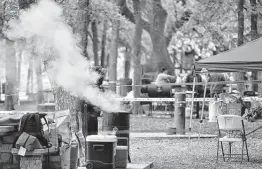  ??  ?? Chris Silva checks his smoker as he prepares brisket, ribs and sausage on Easter Sunday in Brackenrid­ge Park. The parks were open for the holiday this year.