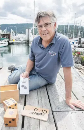  ??  ?? John Denny at Portside Marina with the COVID-19 game, played with wooden dice, that he created. He is donating 50 per cent of the selling price to the Victoria Foundation.