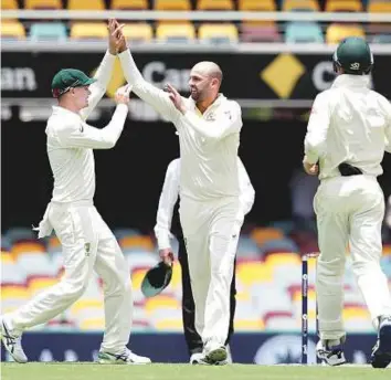  ?? AP ?? Australia’s Nathan Lyon celebrates with Peter Handscomb (left) after claiming the wicket of England’s Chris Woakes during the first Ashes Test in Brisbane yesterday.