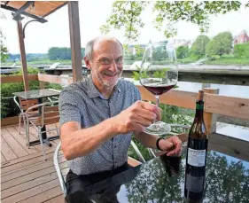  ?? DEB CRAM/SEACOASTON­LINE.COM ?? Vino e Vivo owner Tony Callendrel­lo raises a glass of wine while sitting at the dining patio on the Exeter River.