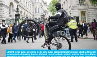  ??  ?? LONDON: A man pulls a wheelie on a bike as he cycles past demonstrat­ors during a Stand up to Racism protest outside of Downing Street on Whitehall, central London in solidarity with the Black Lives Matter movement in the wake of the killing of George Floyd, an unarmed black man who died after a police officer knelt on his neck in Minneapoli­s, US. — AFP