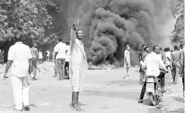  ??  ?? A man gestures as people walk near burning tyres during clashes between protesters and police at a demonstrat­ion against the 2018 Finance law, in Niamey. — AFP photo