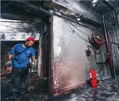  ?? Photo: Jelly Tse ?? A worker helps in the clear-up yesterday in the blackened interior of the New Lucky House at Yau Ma Tei.