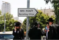 ?? (Ammar Awad/Reuters) ?? HAREDI MEN stand next to a sign pointing toward a recruiting office in Jerusalem in 2017.