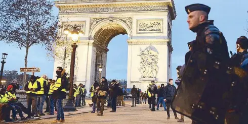  ??  ?? Protestors wearing yellow vests stand near policemen securing the Arc de Triomphe yesterday in Paris, France. AFP