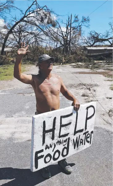  ??  ?? STRANDED: Michael Williams, 70, of Springfiel­d, Florida waves to passing motorists while looking for food and water. Fallen trees blocked his driveway.