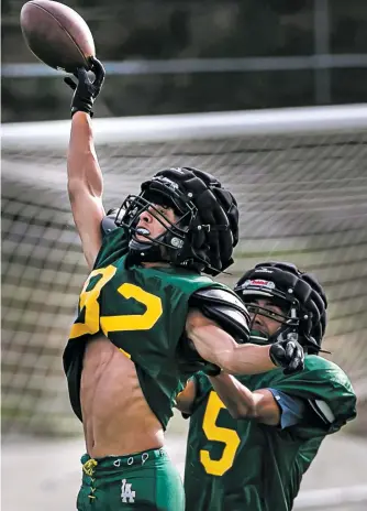  ??  ?? ABOVE: Hilltopper wide receiver Caden Thornton, left, stretches for the ball while running drills during practice Wednesday at Sullivan Field in Los Alamos. Los Alamos players have a new enthusiasm for the team’s run-pass option spread attack.