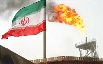  ??  ?? A gas flare on an oil production platform in the Soroush oil fields is seen alongside an Iranian flag in the Persian Gulf, Iran. Iran plans to offer price and tax incentives to private investors to take over idle state projects and help boost the...
