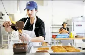  ??  ?? Lisa Smallhover pours icing on a batch of chocolate eclairs at La Gourmandin­e’s new location in Hazelwood.