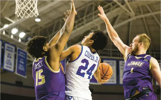  ?? BILLY SCHUERMAN/STAFF ?? Hampton University’s Ford Cooper (24) flies toward the rim before the ball is knocked away by James Madison defenders Jaylen Carey (15) and Noah Freidel (1) during the Dukes’ 88-71 victory Saturday at the HU Convocatio­n Center.