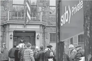  ?? ?? A law enforcemen­t official stands in an entryway to a Silicon Valley Bank branch in Wellesley, Mass., on Monday as customers line up outside.