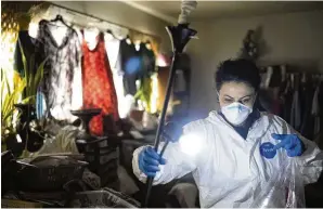  ?? JAE C. HONG / AP ?? Wearing a protective suit, Arusyak Martirosya­n, an investigat­or with the Los Angeles County Public Administra­tor’s office, turns on a lamp while searching through a one-bedroom apartment in 2023 in Los Angeles for clues that might lead to finding family members or relatives of a tenant who died in the hospital with no apparent next of kin.