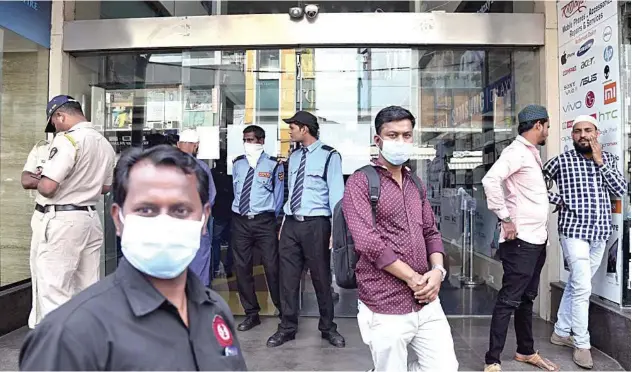  ?? Associated Press ?? ↑
Security guards, customers stand outside a shopping mall closed as a precaution­ary measure against COVID-19 in Mumbai on Sunday.