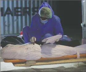  ??  ?? A militia member writes informatio­n on the body wrap of a coronaviru­s victim during a funeral.